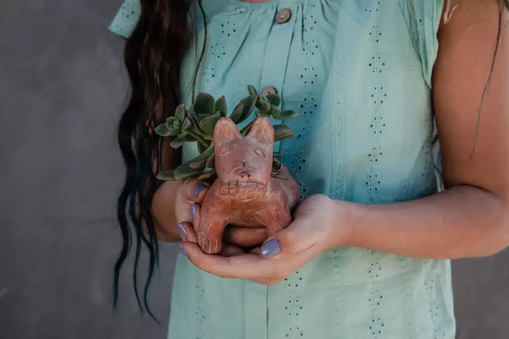 a little girl holding pot shaped like a dog made of clay